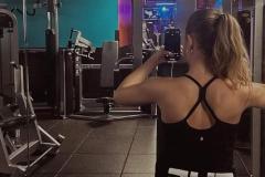 Woman taking a selfie in the gym mirror with fitness equipment.