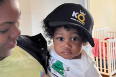 Person holding a baby wearing a KQ baseball cap.
