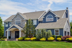 Two-story suburban house with a blue and stone facade and landscaped yard.