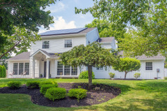 White two-story house with solar panels on roof and landscaped garden.