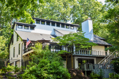 Two-story house with American flag surrounded by trees.