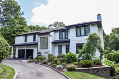 Two-story house with white siding, stone accents, and a curved driveway.