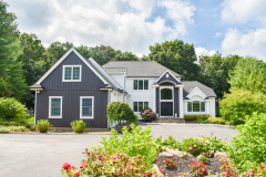 Two-story house with dark and white siding, arched entryway, surrounded by greenery.